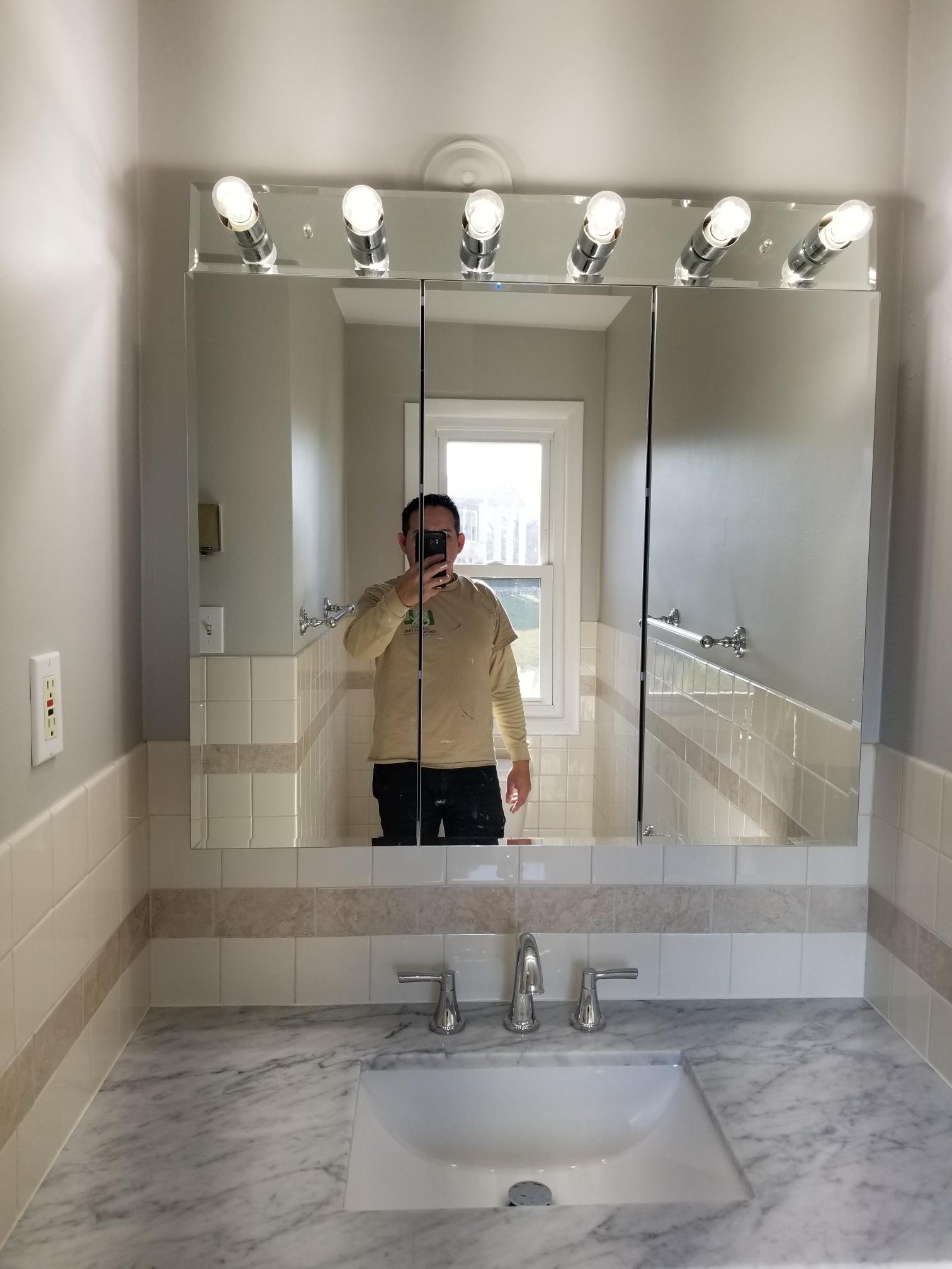 Person holding a smartphone taking a selfie in a bathroom mirror, revealing a marble countertop and tiled walls