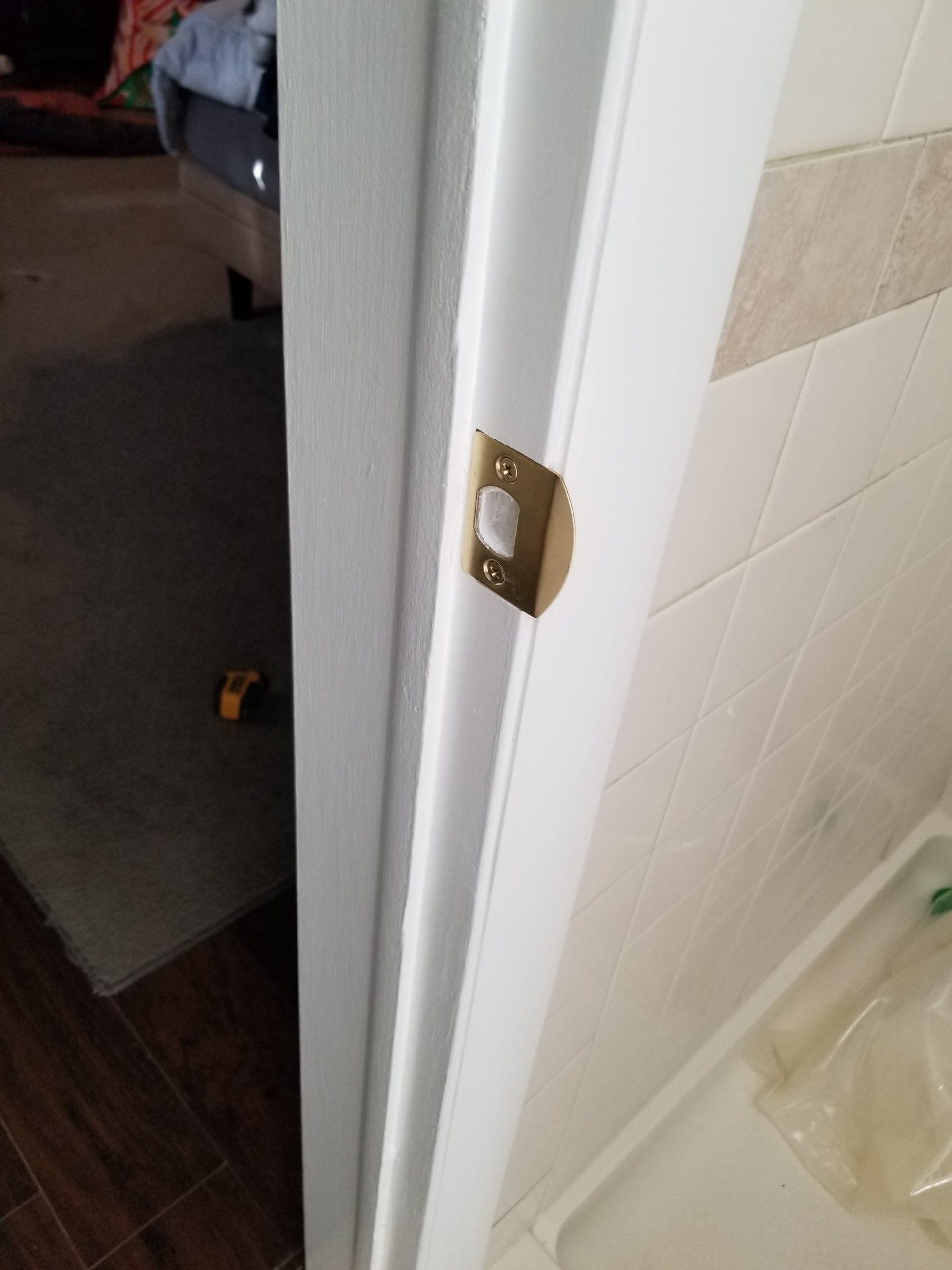 Close-up of a newly installed silver door striker plate on a white door frame with a visible screwdriver