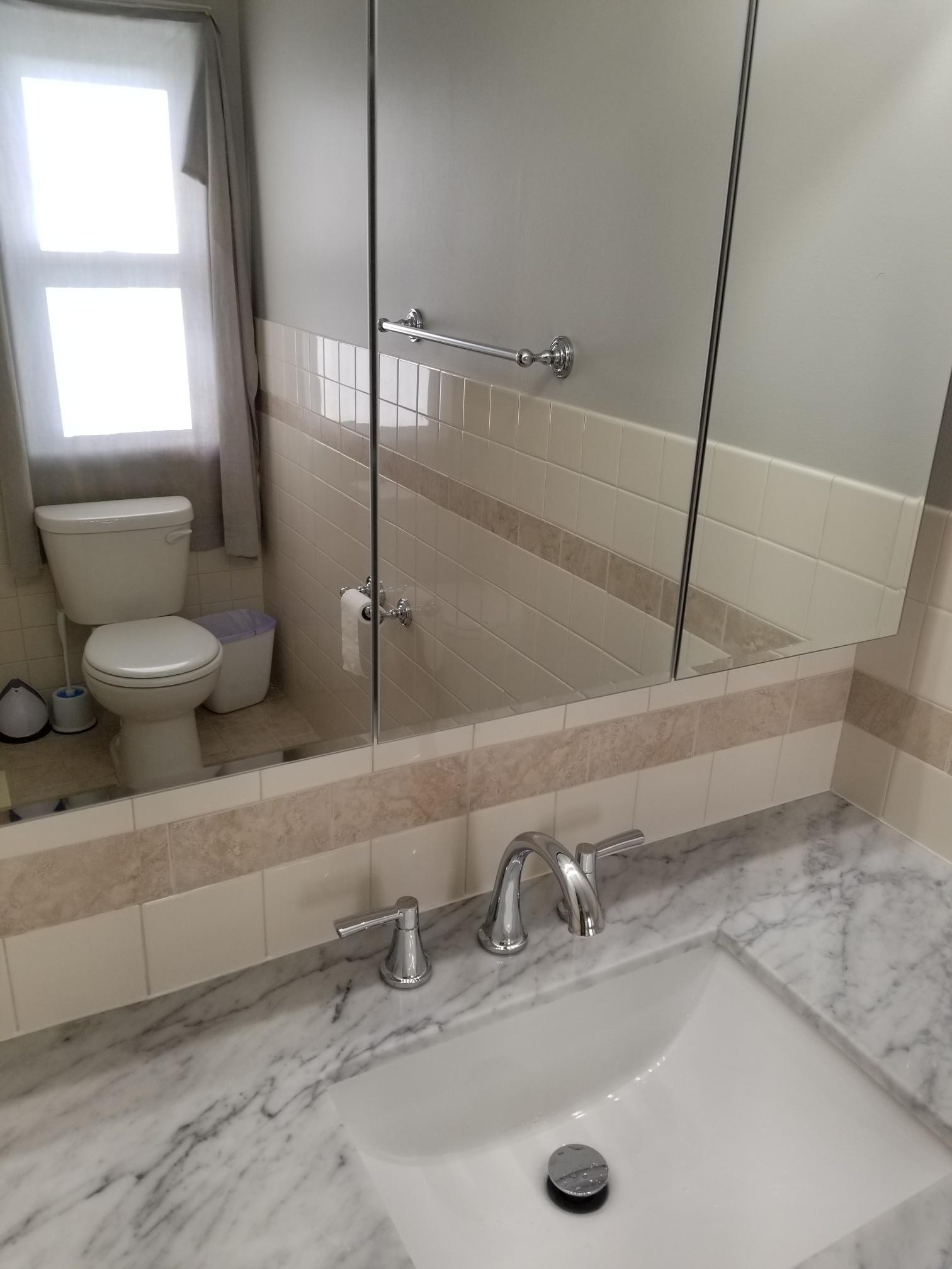 Modern bathroom with marble countertop and square vessel sink, reflecting a well-lit interior and tiled walls.