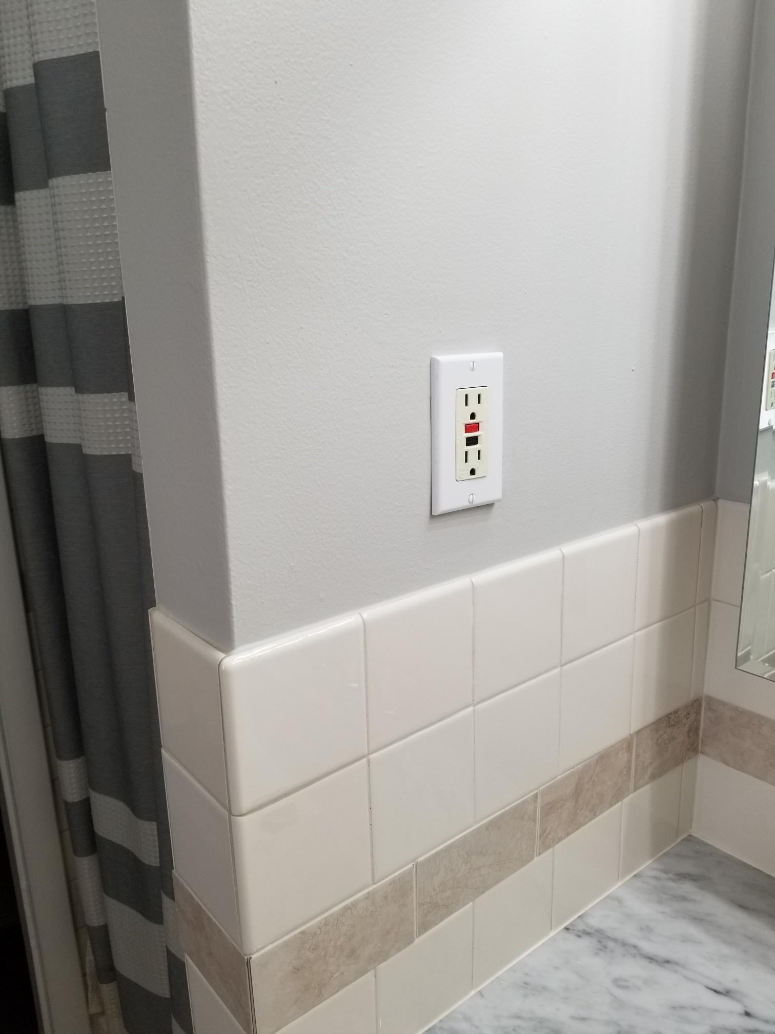 Wall-mounted GFCI outlet above a tiled bathroom backsplash, indicative of modern safety standards in home design