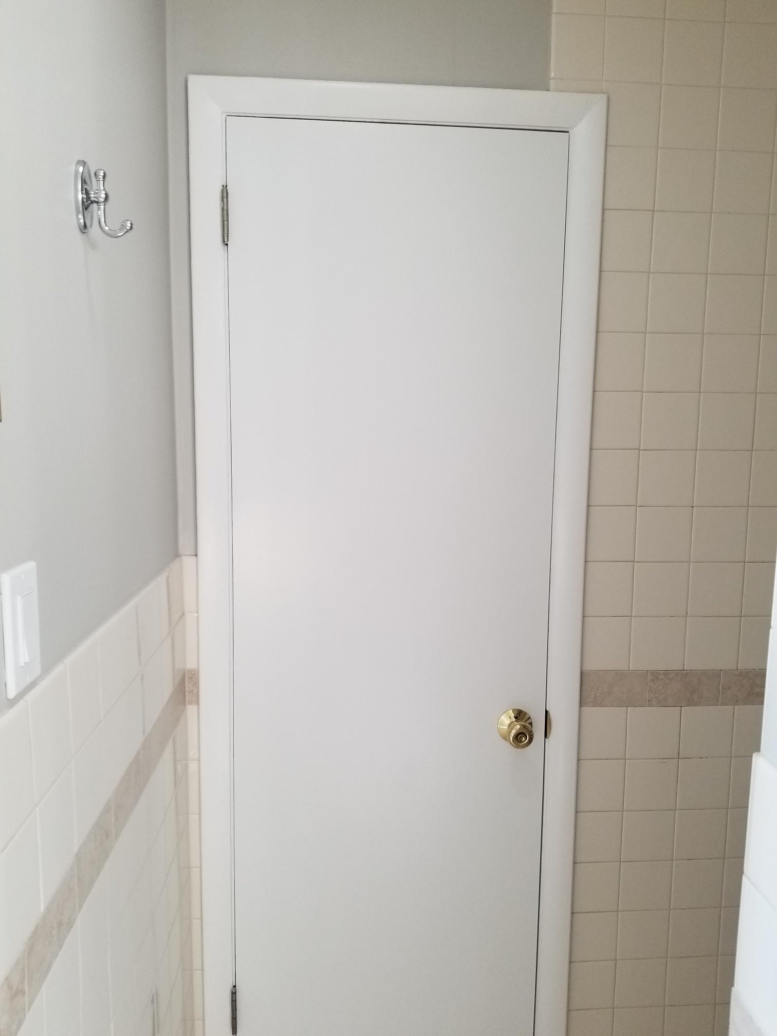 Interior door in a bathroom with a golden knob and lock, contrasting against the white door and tiled wall