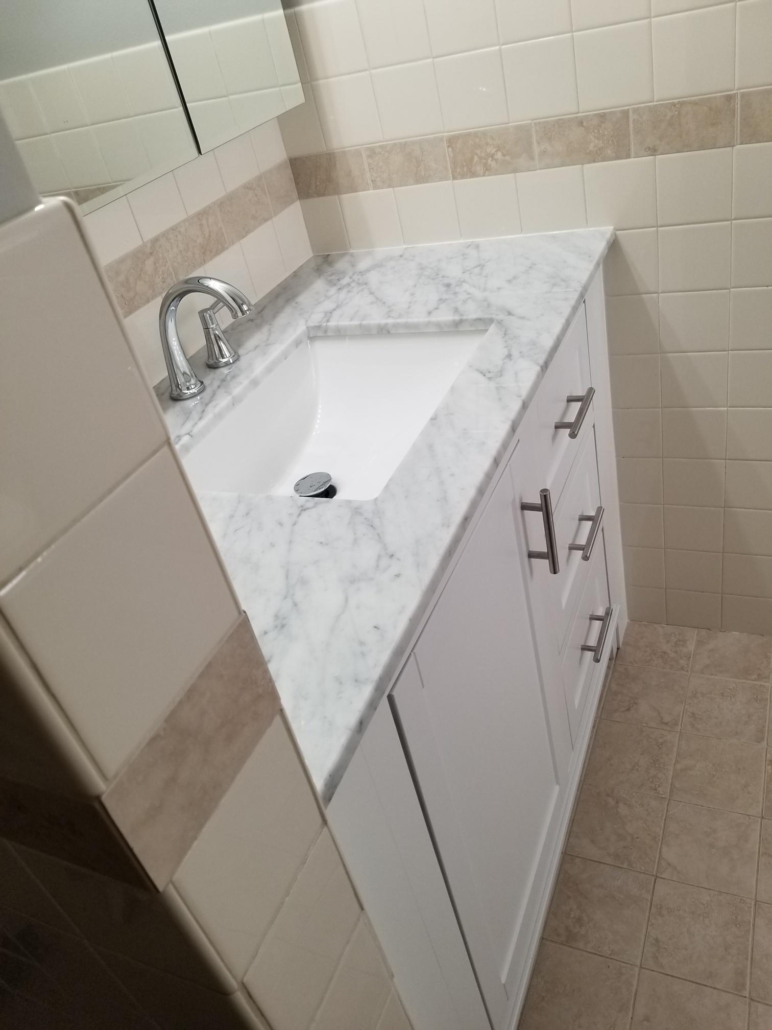 Angled view of a modern bathroom vanity with a marble top and white cabinetry, showcasing clean lines and design