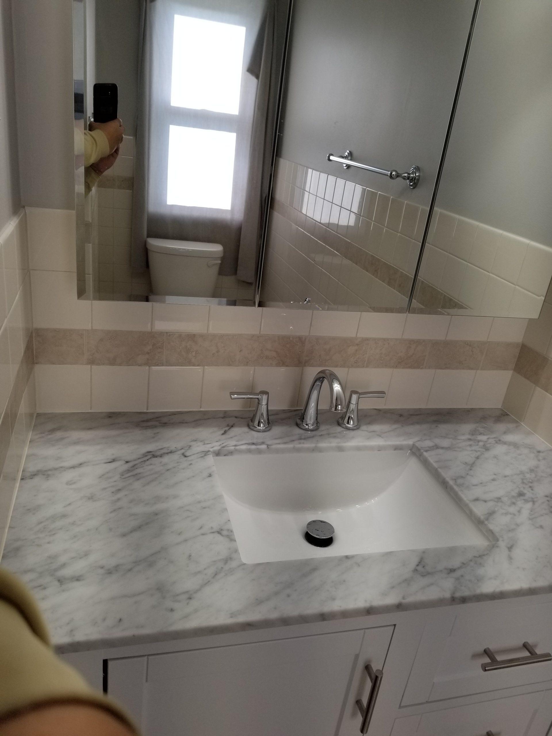 Elegant bathroom mirror reflecting a bright window and showing a part of a white toilet and tiled bathtub
