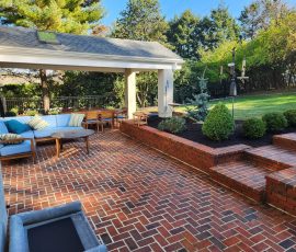 large backyard patio made of uniform bright red bricks with matching retaining walls and steps