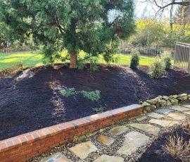 natural stone path filled in with pebbles and bordered by large flowerbeds with shrubs and trees