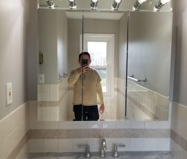 Person holding a smartphone taking a selfie in a bathroom mirror, revealing a marble countertop and tiled walls