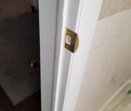Close-up of a newly installed silver door striker plate on a white door frame with a visible screwdriver