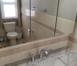Modern bathroom with marble countertop and square vessel sink, reflecting a well-lit interior and tiled walls.
