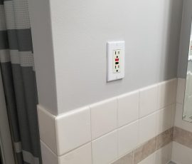 Wall-mounted GFCI outlet above a tiled bathroom backsplash, indicative of modern safety standards in home design