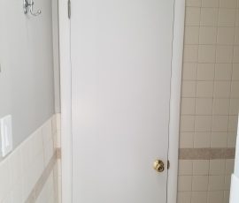 Interior door in a bathroom with a golden knob and lock, contrasting against the white door and tiled wall