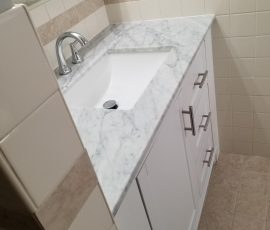 Angled view of a modern bathroom vanity with a marble top and white cabinetry, showcasing clean lines and design