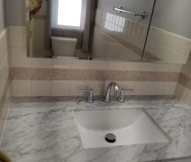Elegant bathroom mirror reflecting a bright window and showing a part of a white toilet and tiled bathtub